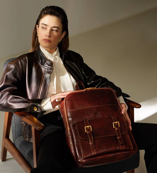 A woman in a stylish leather jacket sits with an elegant brown leather backpack on her lap, exuding sophistication.